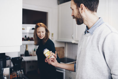 Man giving food jar to woman in kitchen at home