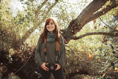 Portrait of smiling young woman standing against trees