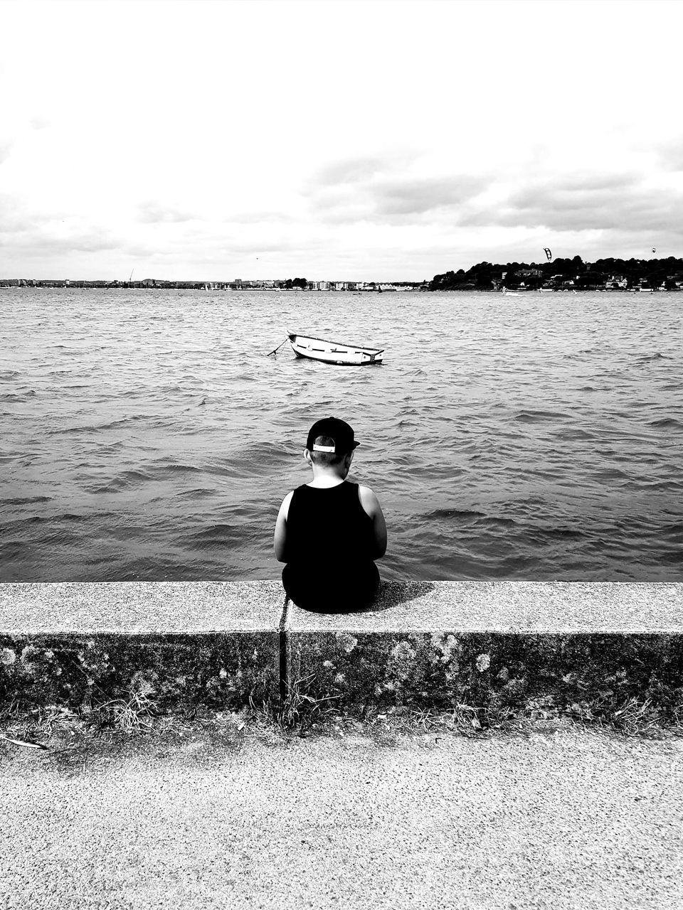 REAR VIEW OF MAN SITTING ON SHORE AGAINST SKY