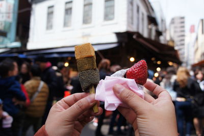 Cropped image of hands holding dessert and fruit in city