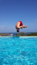 Man jumping in swimming pool against clear blue sky