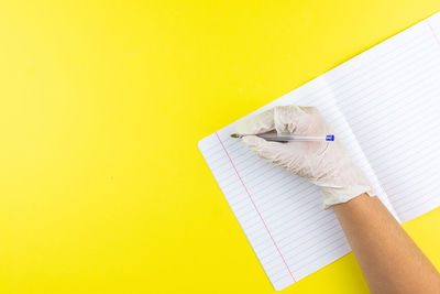 Human hand holding paper against yellow wall