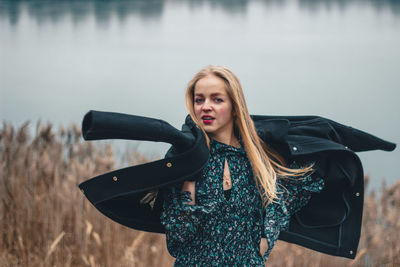 Portrait of beautiful woman wearing jacket standing by lake