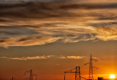 Low angle view of silhouette electricity pylon against dramatic sky