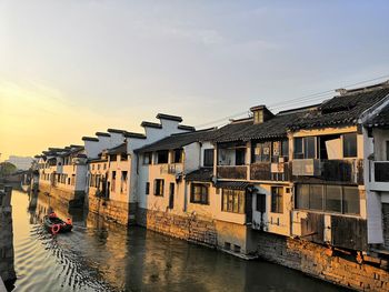 Houses by river against buildings in city against sky