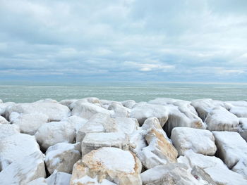 Groyne at sea shore against cloudy sky