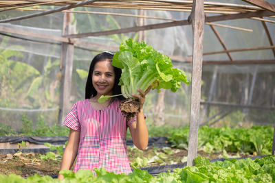 Portrait of smiling young woman holding lettuce in nursery