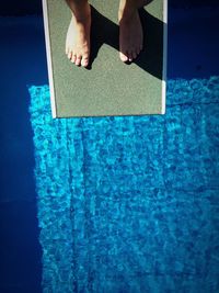 Low section of man standing on diving platform over swimming pool