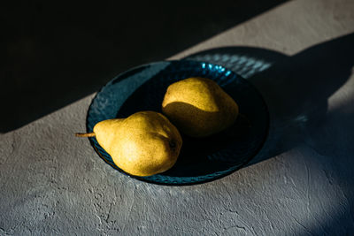Close up one ripe yellow pear in blue glass plate on grey background. modern minimal still life