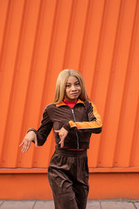 Cheerful african american woman in sportswear dancing in the street on an orange background