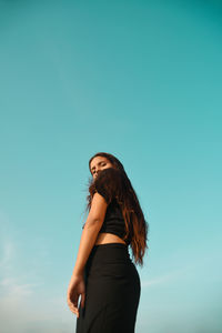 Low angle view of woman standing against clear blue sky