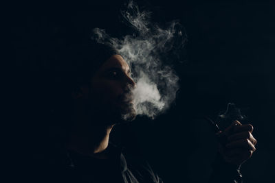 Man smoking pipe against black background