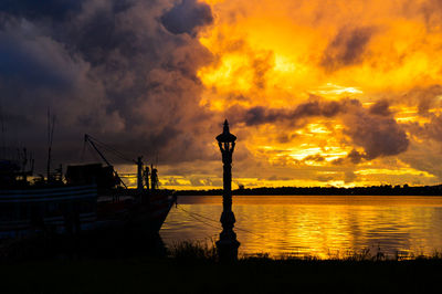 Silhouette boat moored at seashore against cloudy sky during sunset