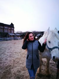 Portrait of young woman with horse on field during sunset