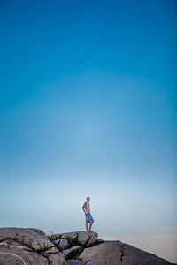 Woman standing on rock against blue sky