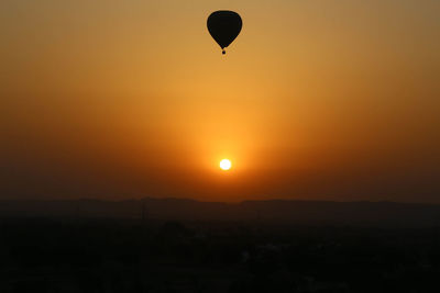 Silhouette hot air balloon flying over landscape against orange sky