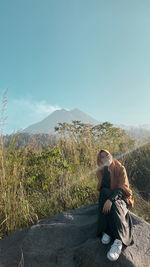 Man sitting on mountain against sky