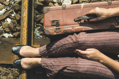 Low section of woman with suitcase sitting on railroad track