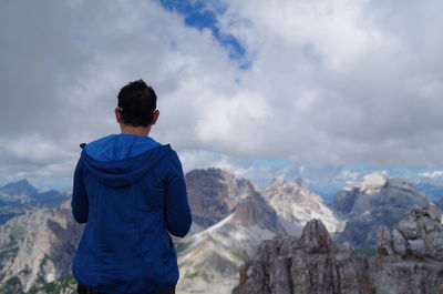 Rear view of mature man standing on mountain against cloudy sky