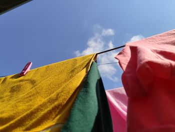 Low angle view of multi colored laundry drying on clothesline against blue sky