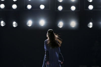 Low angle view of woman standing by illuminated lights at night