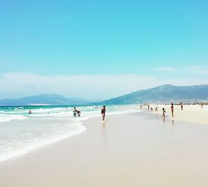 People at beach against blue sky during sunny day