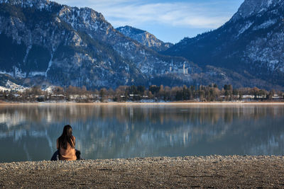 Rear view of woman sitting by lake against mountains