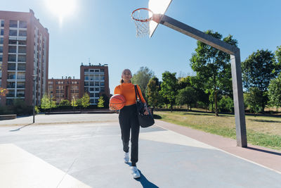 Young sportswoman with basketball walking in sports court