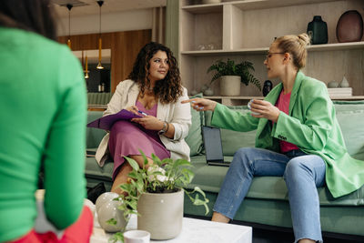 Mature female boss assisting female colleague while sitting on sofa during meeting at office