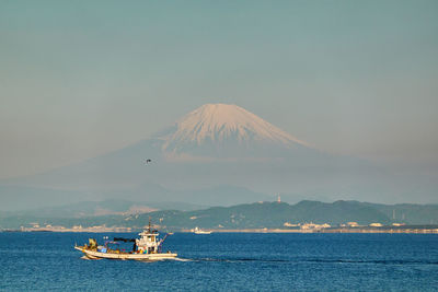 Boat sailing on sea by snowcapped mountain against sky