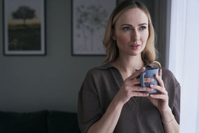 Woman holding coffee cup looking away at home