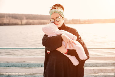 Portrait of woman carrying daughter while standing against sea