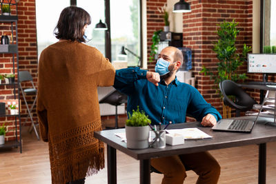 Business people wearing mask bumping elbow at office