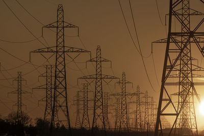 Low angle view of electricity pylon against sky at sunset