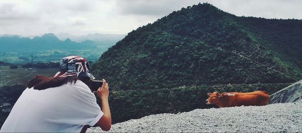 Man photographing woman standing on mountain against sky