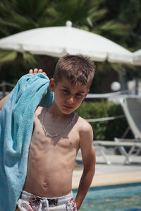 Shirtless boy with towel looking down while standing at poolside