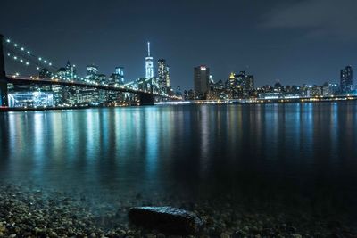 Illuminated city by river against sky at night