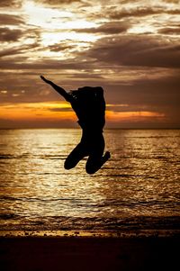 Silhouette man jumping on sea against sky during sunset