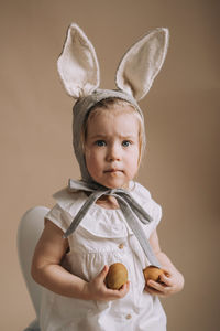 Toddler baby girl in funny hat with ears sitting with eggs in her hand