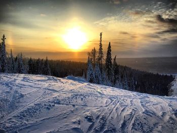 Snow covered landscape against sky during sunset