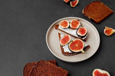 Triangular sandwiches with figs, cream cheese on black bread with seeds on flat porcelain plate