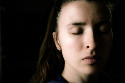 Close-up young woman with eyes closed against black background