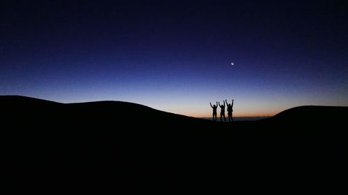 Silhouette people on landscape against clear sky at night