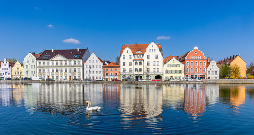 Buildings by river against clear blue sky