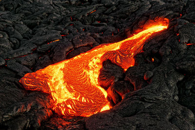 A lava flow emerges from a rock column and pours into a black volcanic landscape