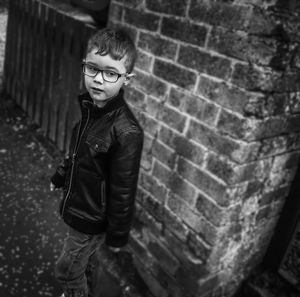 Cute boy wearing eyeglasses while standing against brick wall