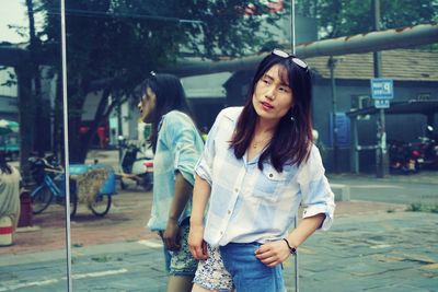 Mid adult woman looking away while standing by window in city