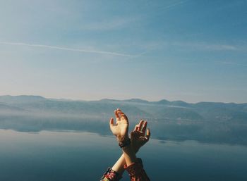 Full length of hand on lake against sky