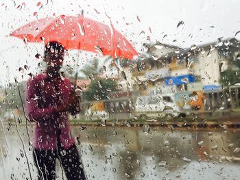 Man carrying umbrella seen through wet glass window