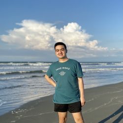 Portrait of young man standing at beach against sky